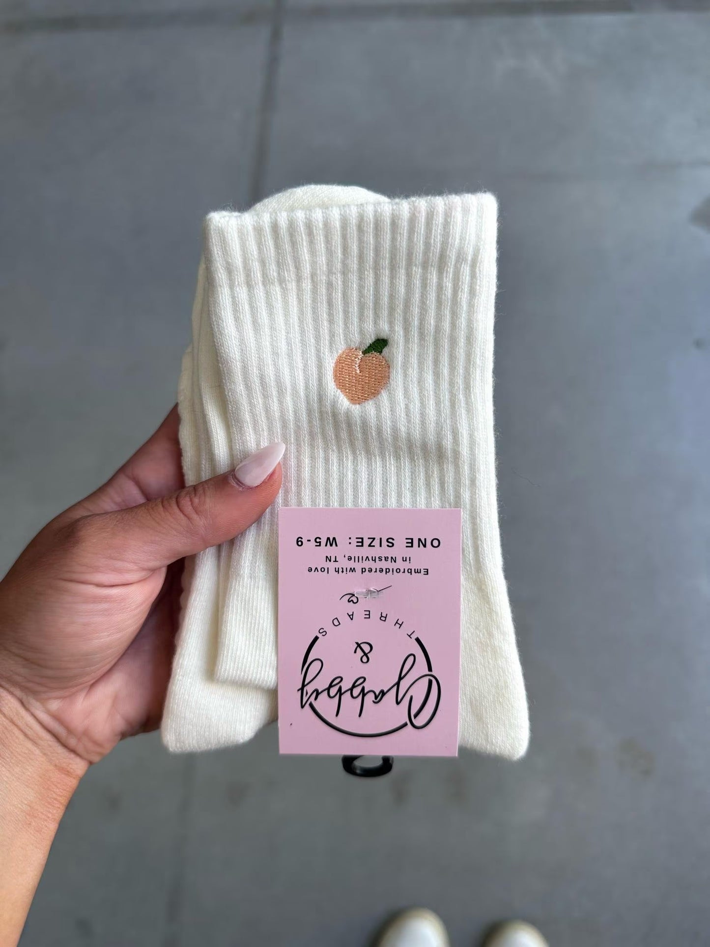 White grip socks with a peach embroidered on them held by a hand, against a gray background