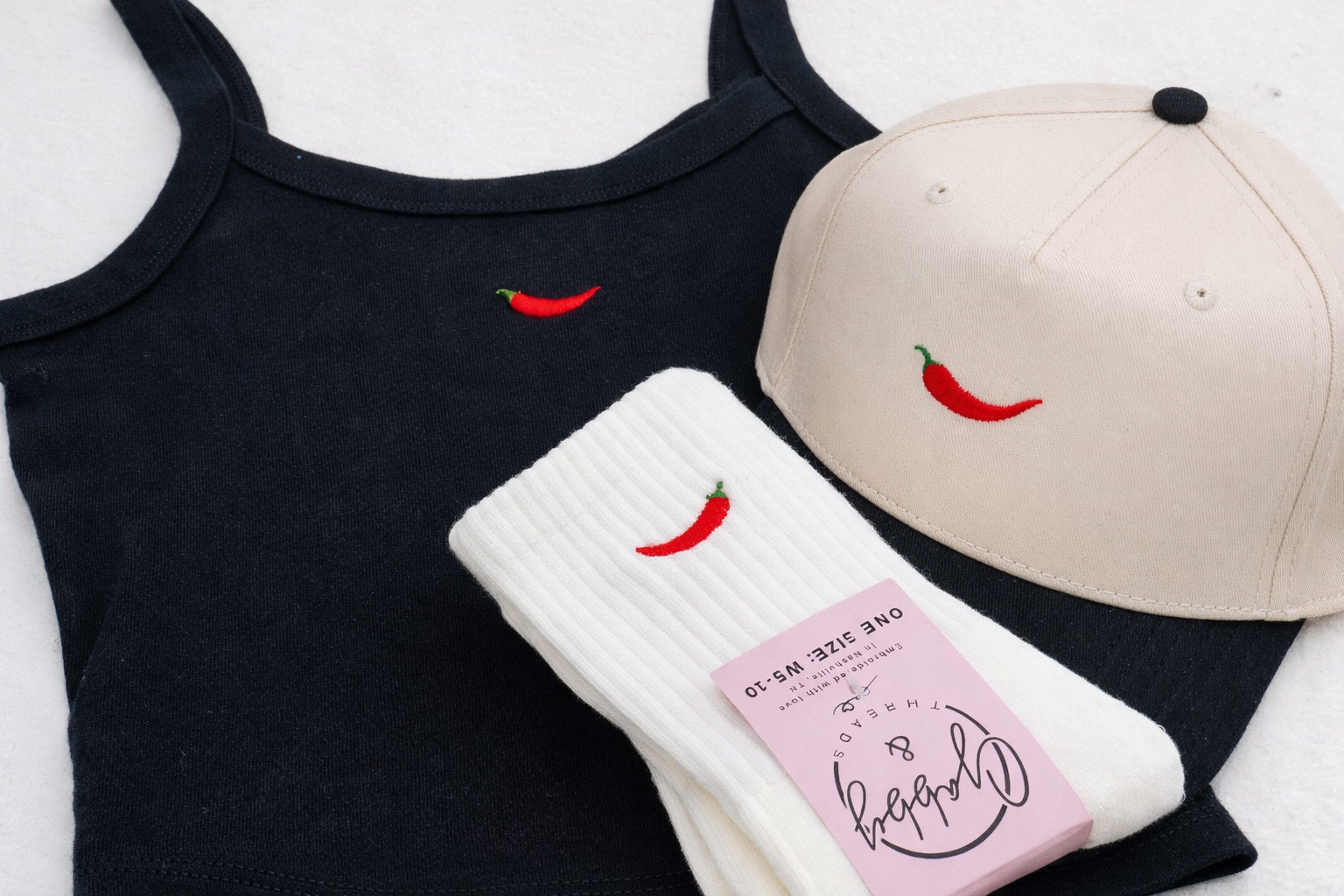 Black tank top, beige cap, and white socks with red chili pepper design on a white background