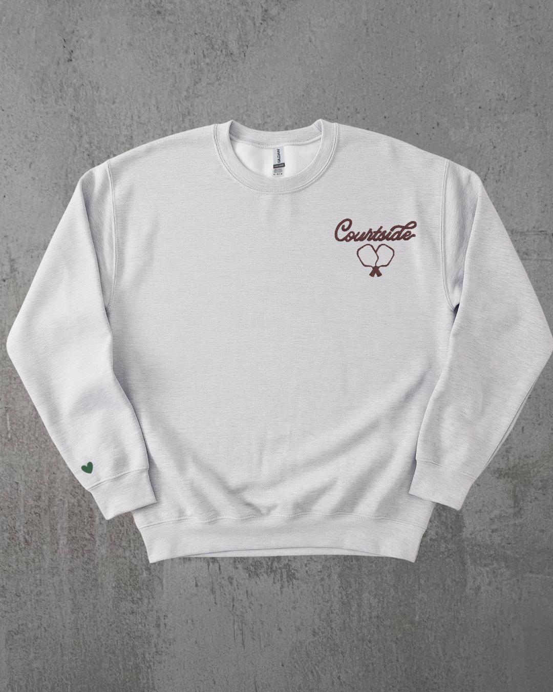 a grey crewneck with an embroidered pickleball paddle against a grey background