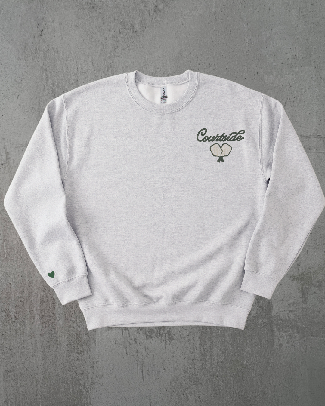 a grey crewneck with an embroidered pickleball paddle against a grey background