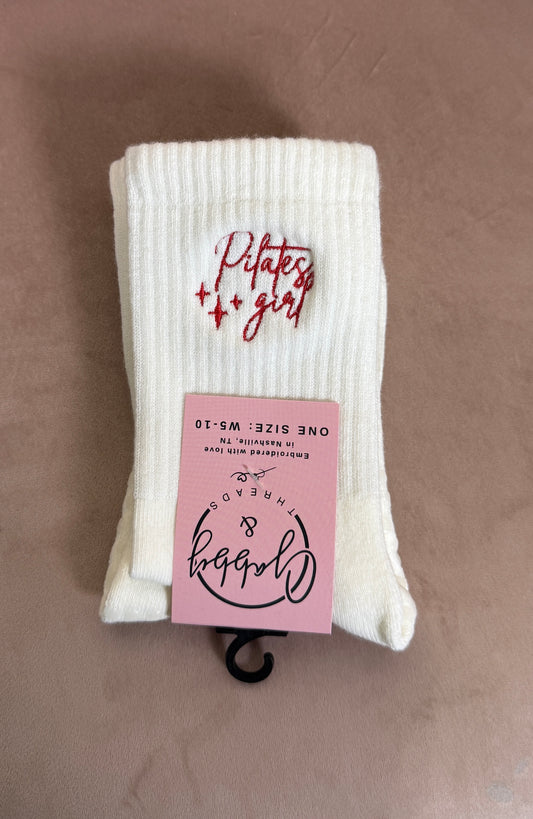 a pair of white grip socks with the words "pilates girl" embroidered on them 