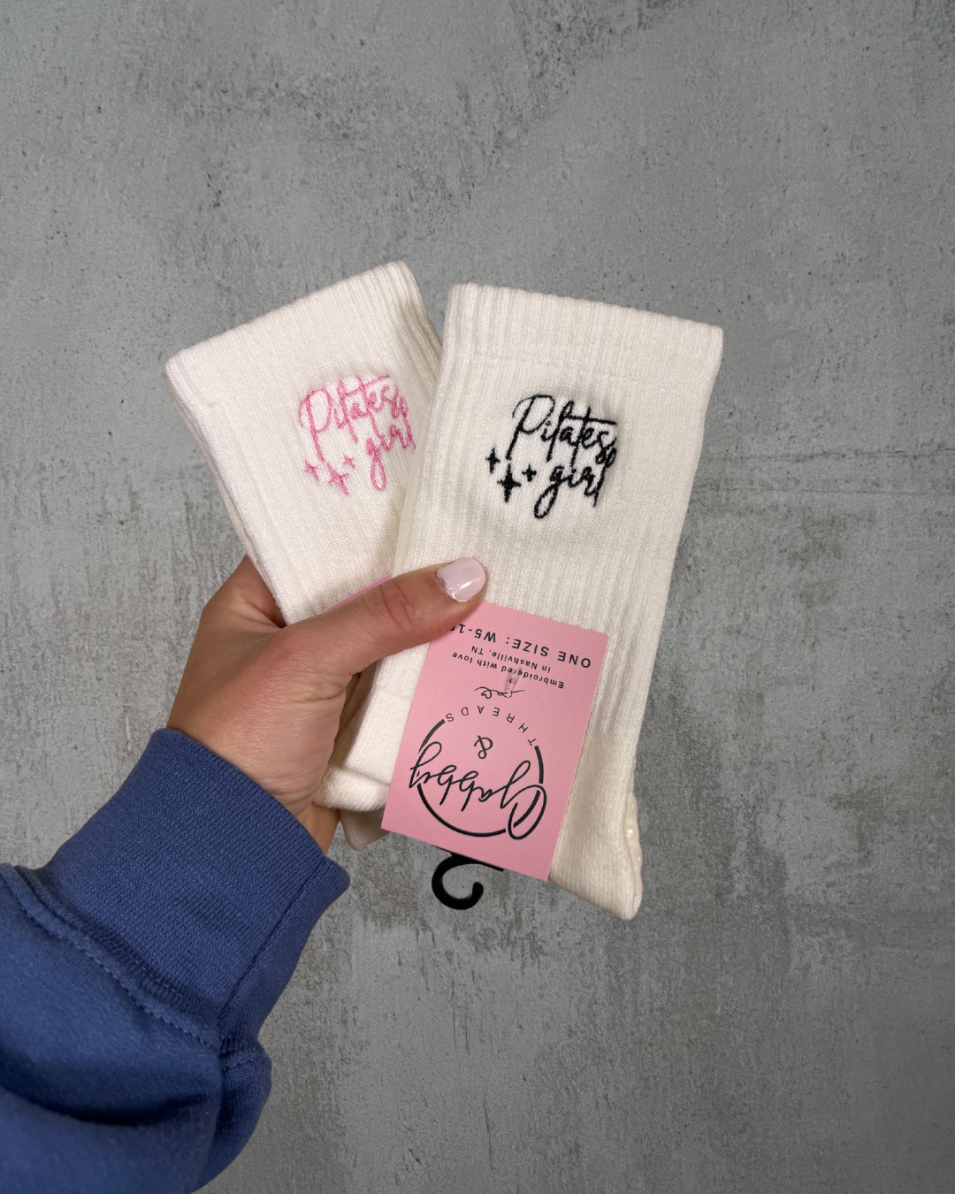 Two white grip socks with text held by a hand against a gray background