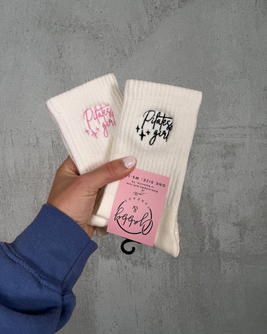 Two white grip socks with text held by a hand against a gray background