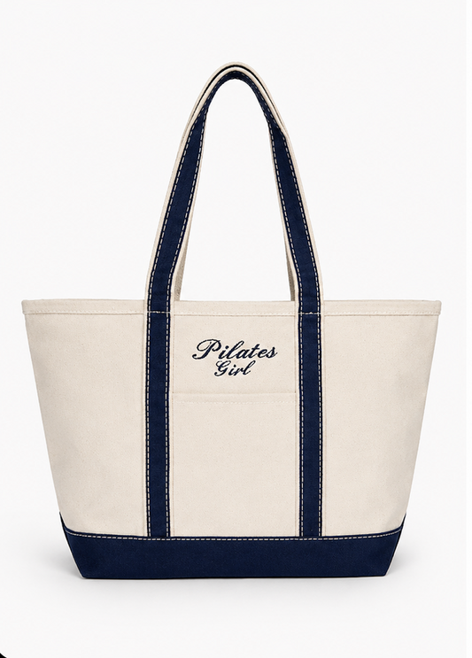 canvas tote bag with navy trim with the words "pilates girl" embroidered on it in navy thread