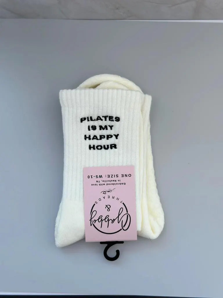 White grip socks with 'Pilates is my happy hour' text on a gray background