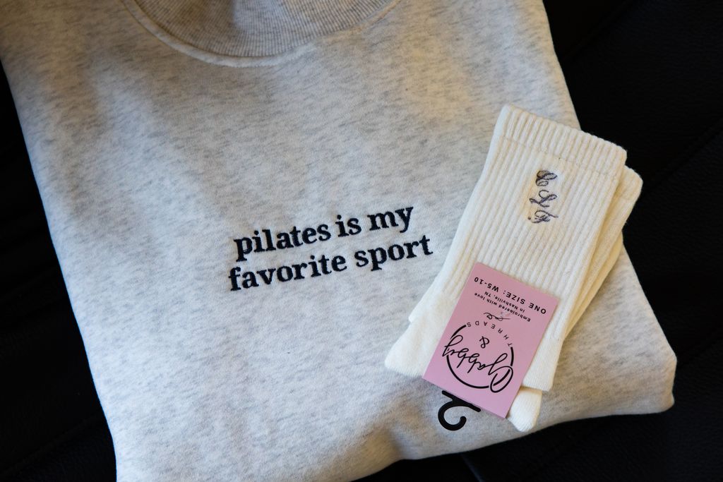 a folded mockneck sweatshirt featuringt the words "lagree is my favorite sport" with a pair of grip socks laying on top 