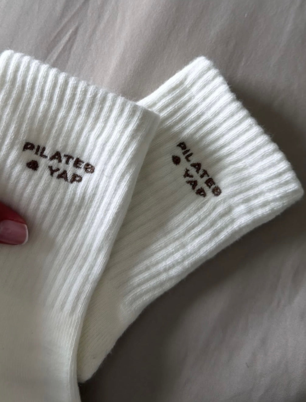 white grip socks with the words "pilates & yap" embroidered on them in brown thread against a white background