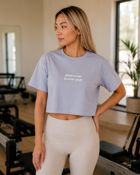 a women is in a pilates studio wearing a cropped tshirt that says "pilates is my favorite sport"