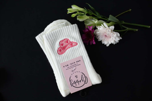 a pair of white socks with a pink embroidered cowgirl hat 