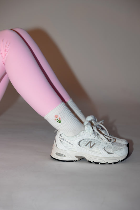 a person is wearing a pair of pink leggings, new balance sneakers and white grip socks for pilates with an embroidered flower on them