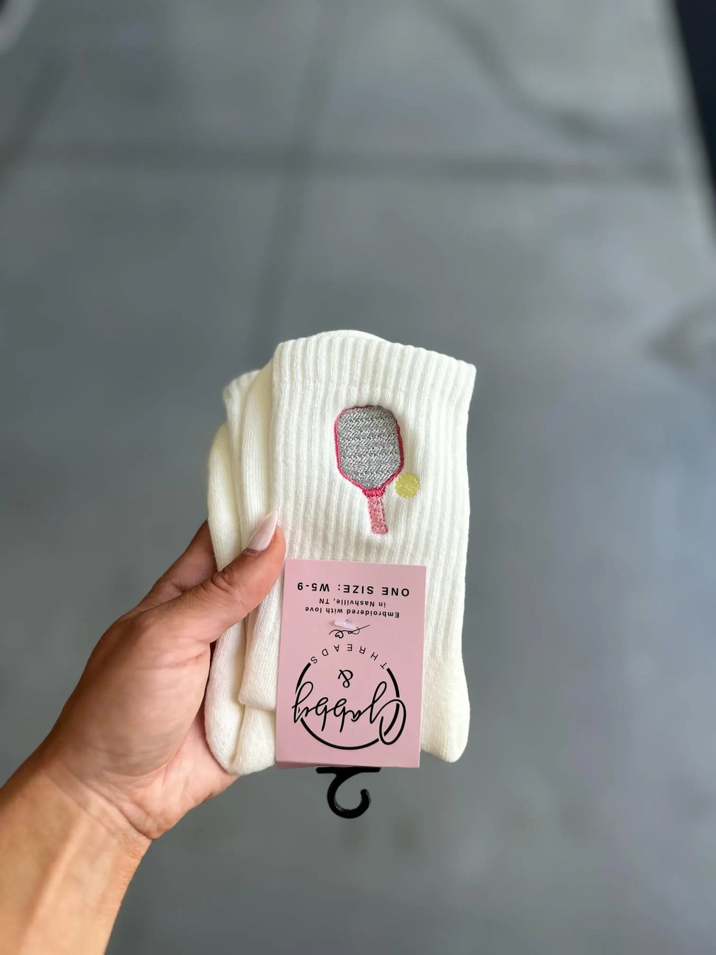 White sock with a pink pickleball paddle held by a hand against a gray background