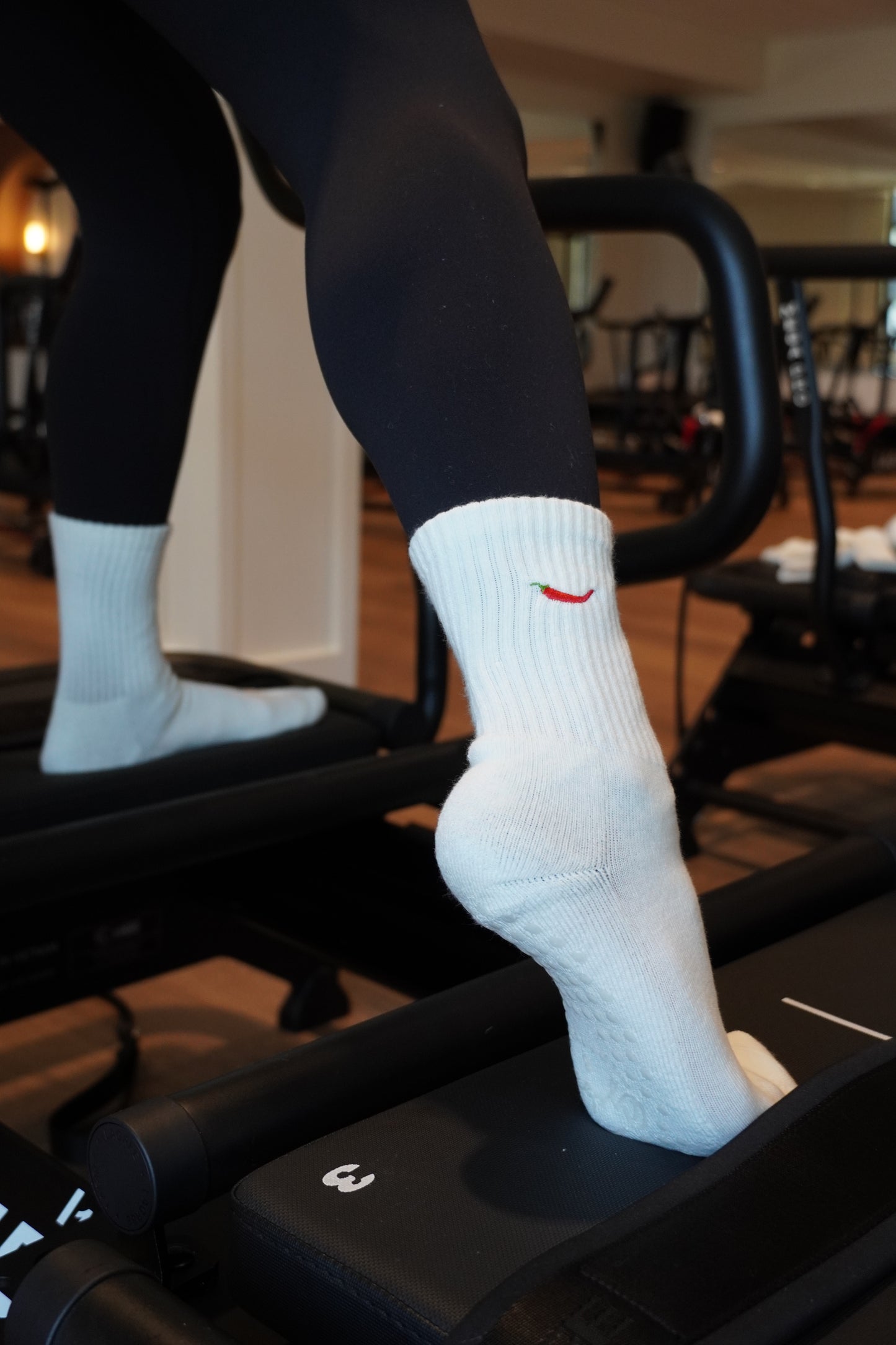 a person is working out on a reformer and wearing white grip socks with a pepper embroidered on them