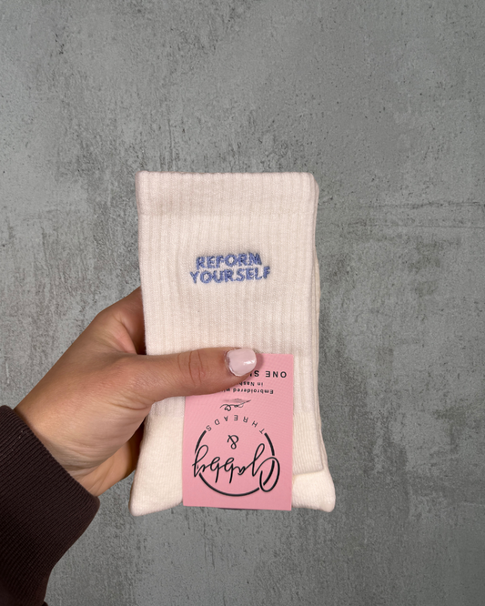 a pair of white grip socks with the text "reform yourself" embroidered on them