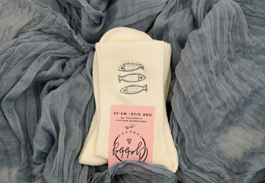 a pair of white grip socks with sardines embroidered on them