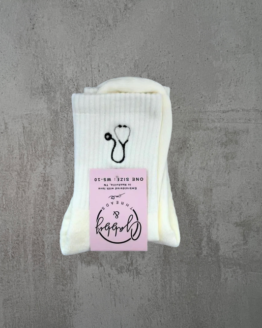 a pair of white grip socks with a stethoscope embroidered on it against a grey background