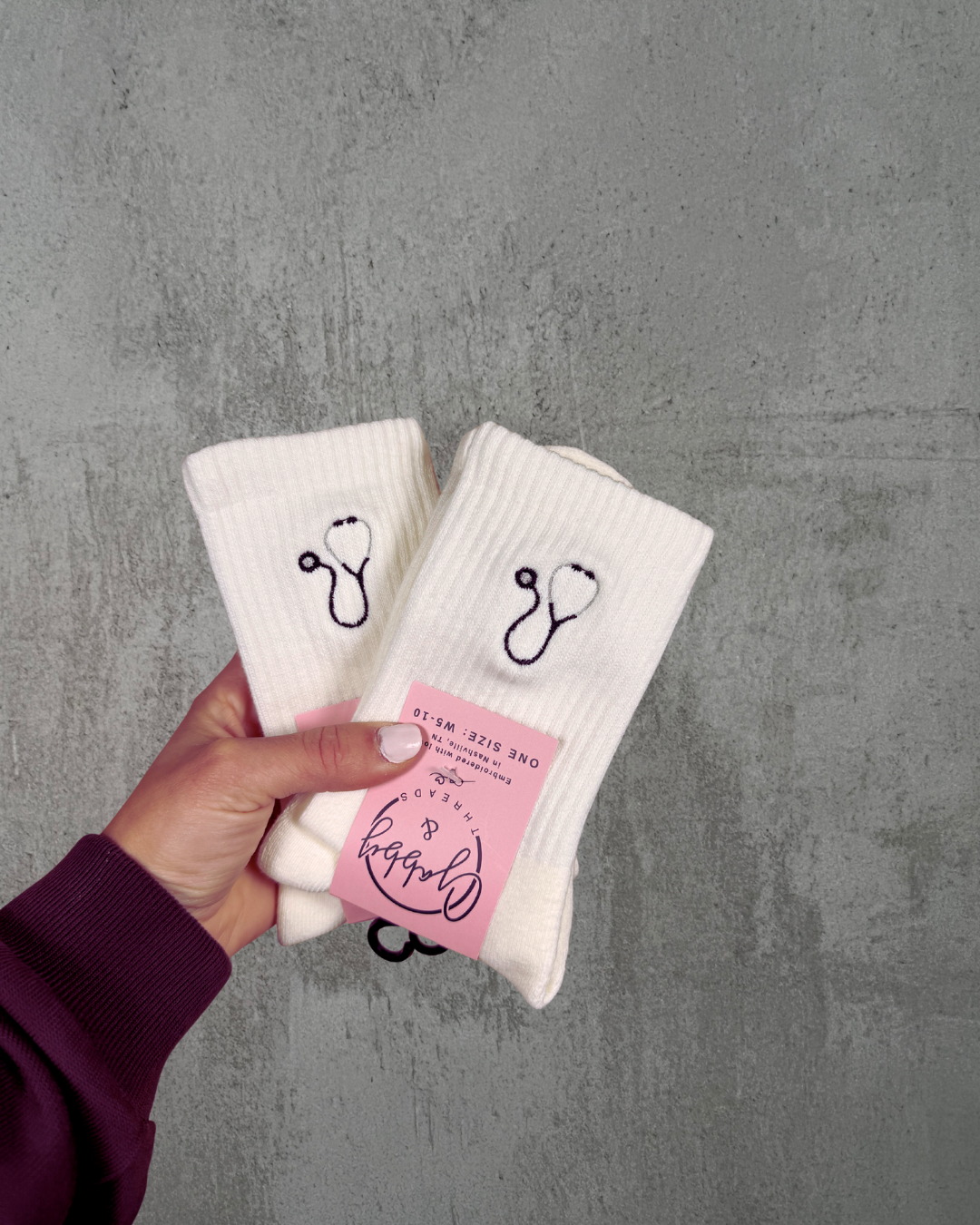a hand holds up two pairs of socks with black stethoscopes embroidered on them against a gray background