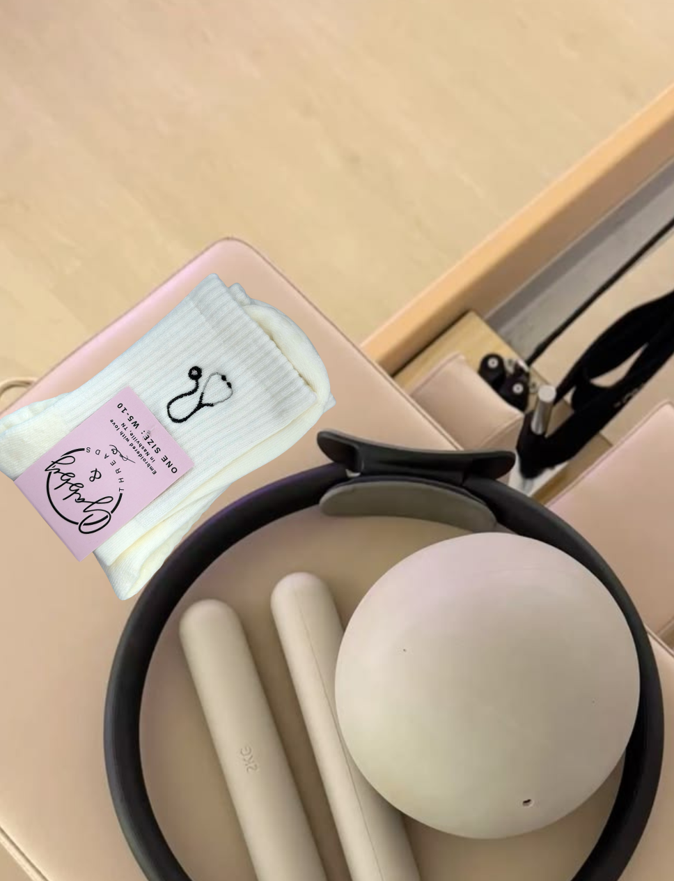 a pair of white grip socks with an embroidered stethoscope on them placed on a pilates reformer next to workout equipment