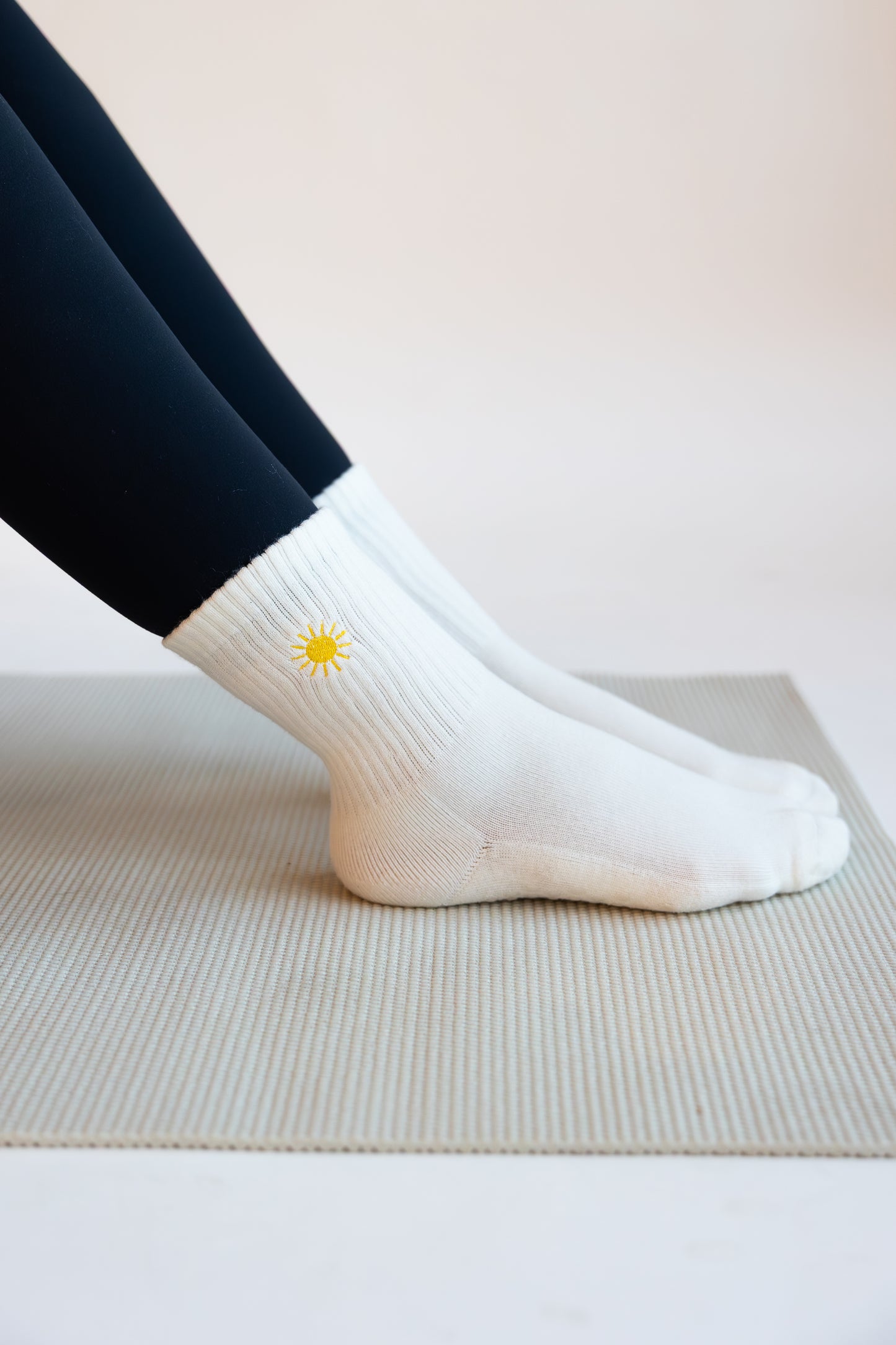 White pilates socks with a yellow sun embroidered on them worn by a person on a light background