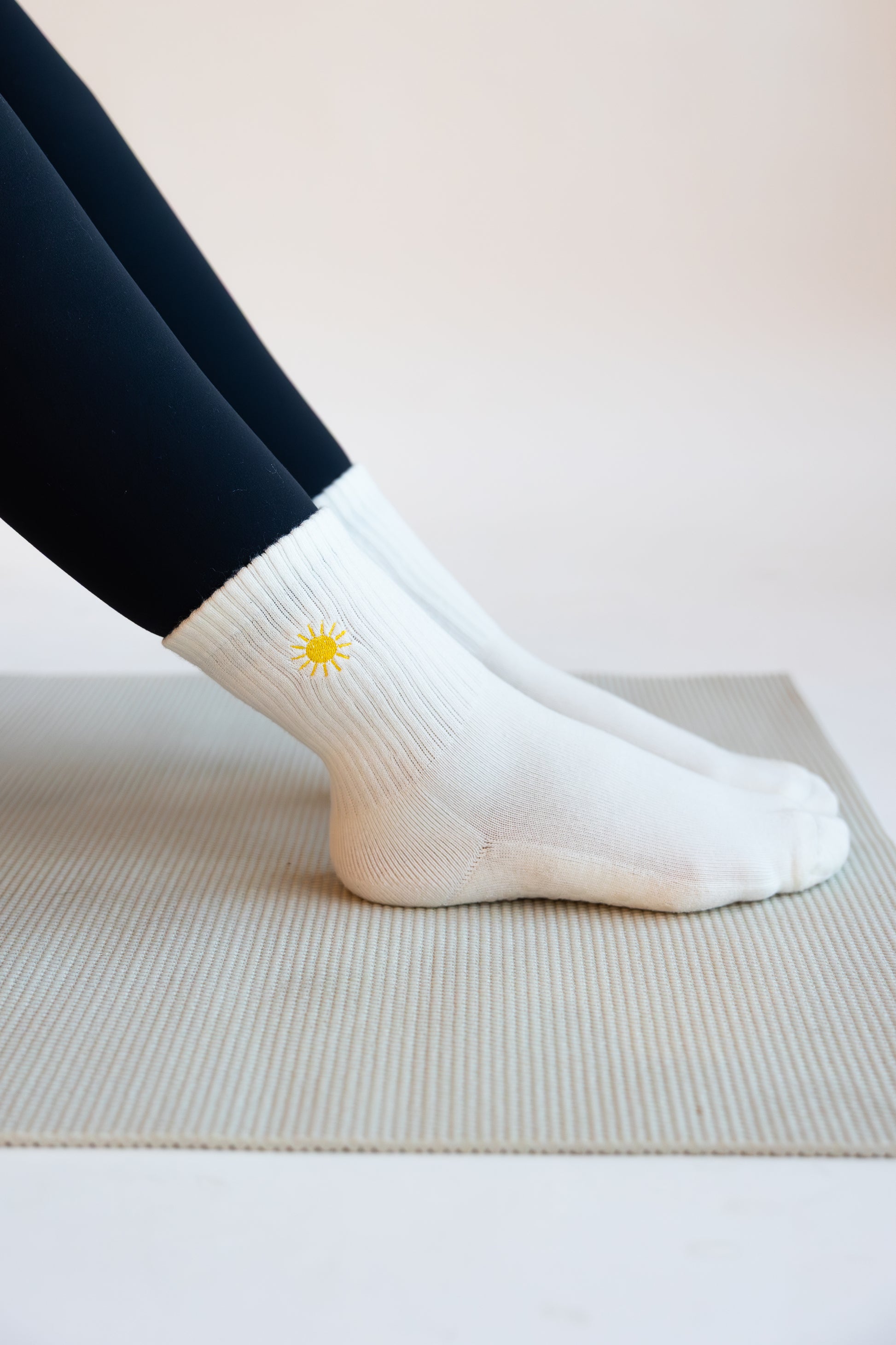 White pilates socks with a yellow sun embroidered on them worn by a person on a light background