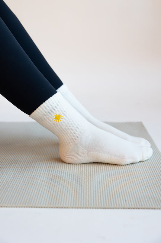White pilates socks with a yellow sun embroidered on them worn by a person on a light background