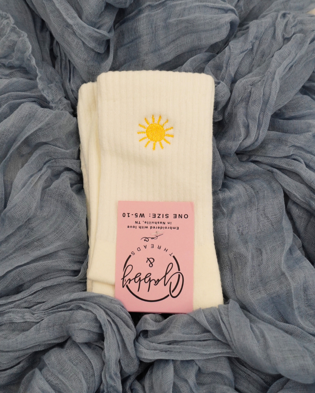a pair of white grip socks with a yellow sun embroidered on them laying against a blue textured background
