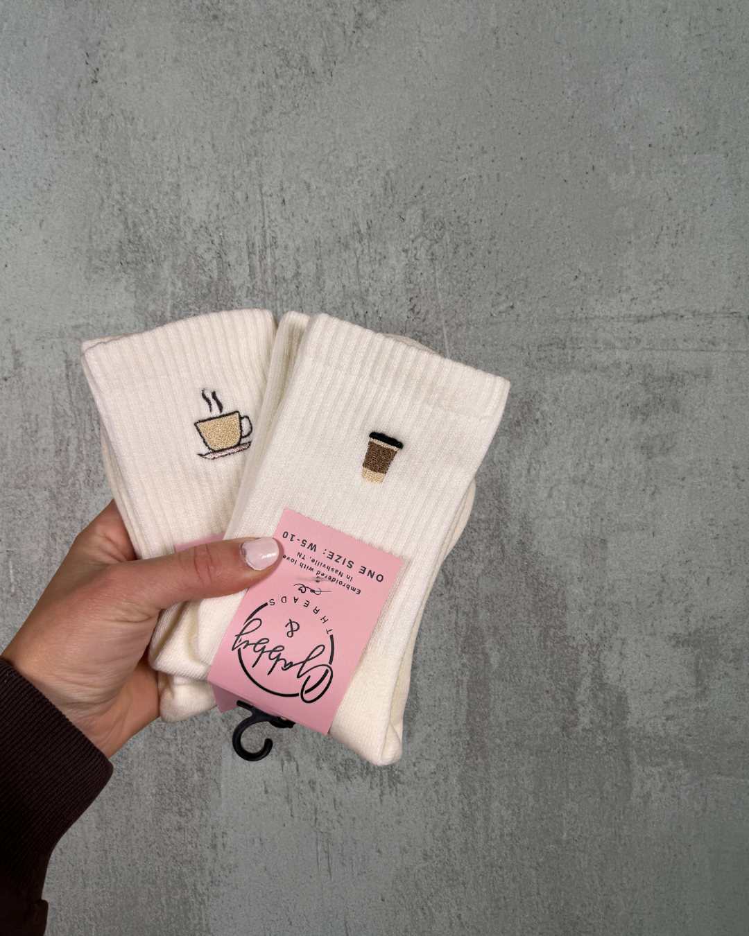 two pairs of white grip socks, one pair of socks has an embroidered coffee cup and the other one has an embroidered to go coffee cup