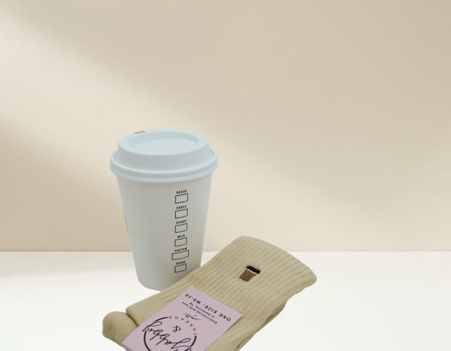 a pair of pilates socks that are embroidered with a coffee cup, sitting next to a coffee cup, against a tan background