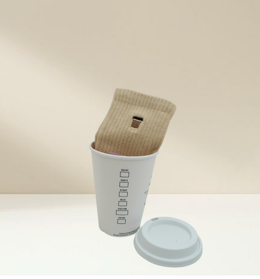 a pair of pilates socks that are embroidered with a coffee cup, sitting inside a coffee cup, against a tan background