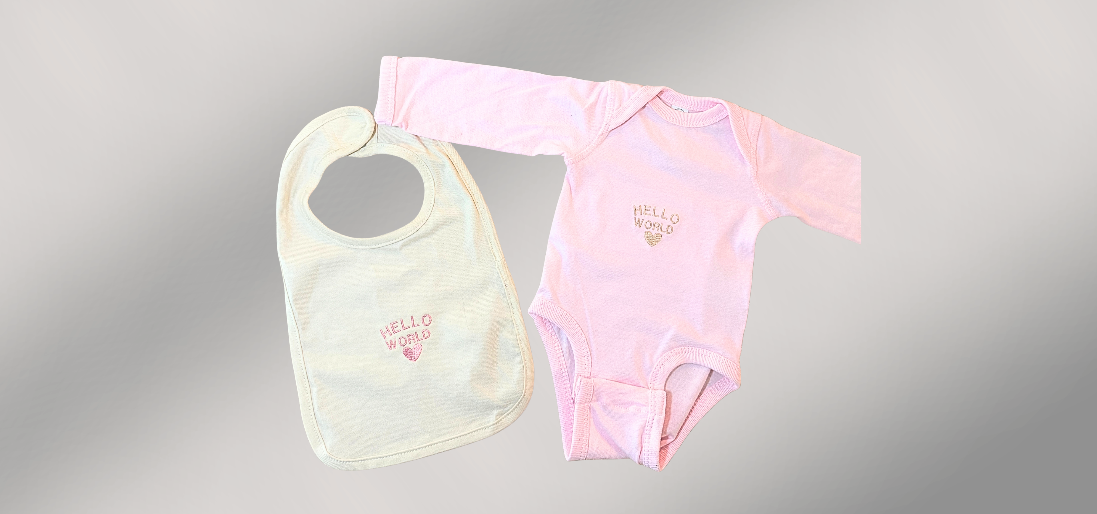 Pink baby bodysuit and bib with 'Hello world' print on a gray background