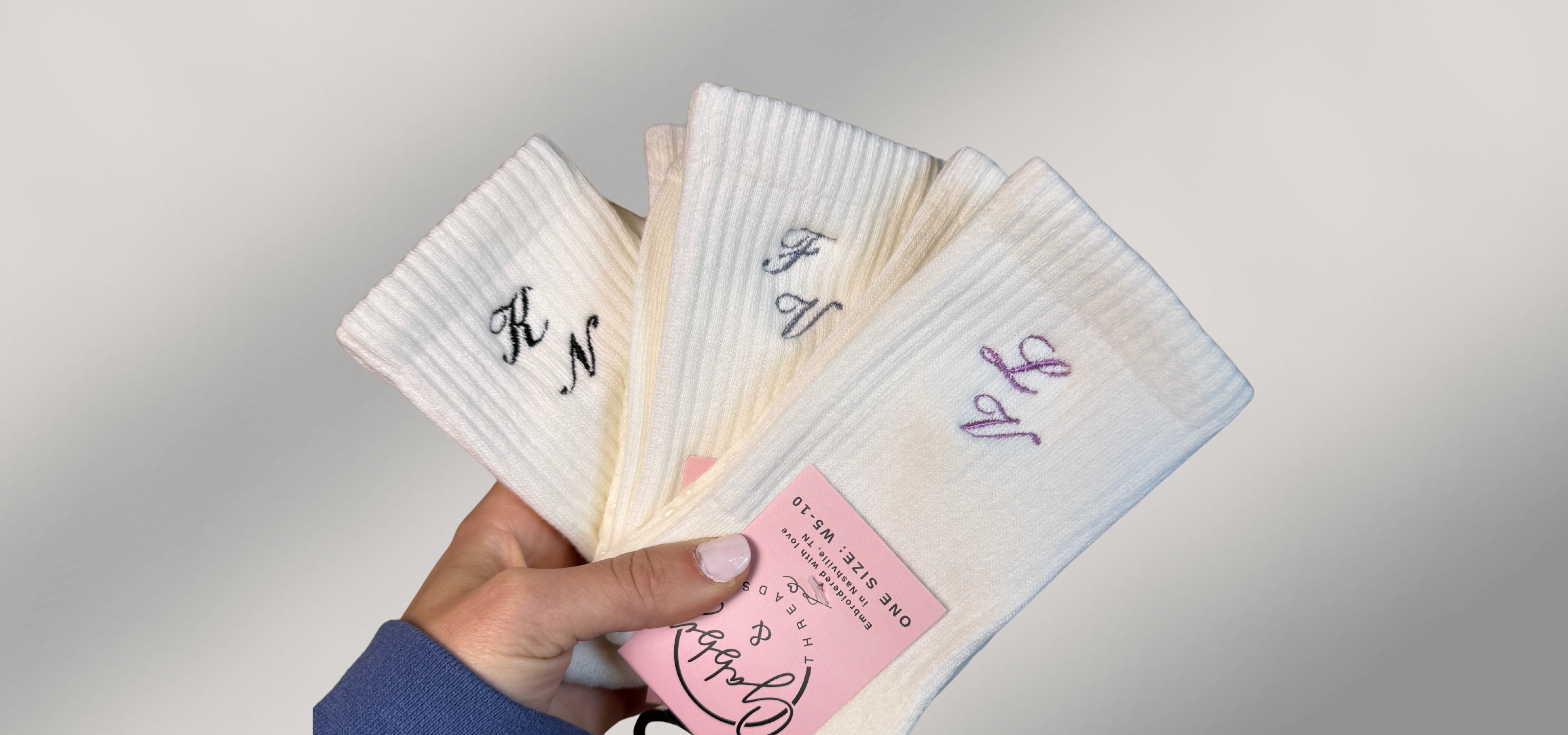 Hand holding a set of personalized socks with monogram initials on a grey background