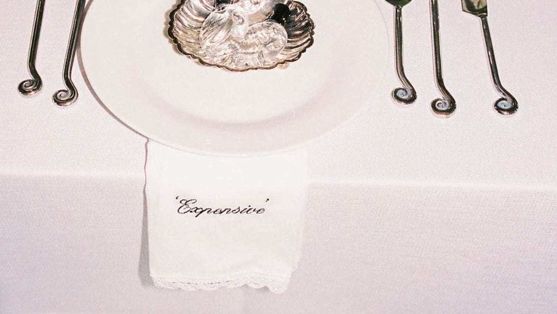 Elegant table setting with silverware, glassware, and a custom embroidered napkin on a white tablecloth.