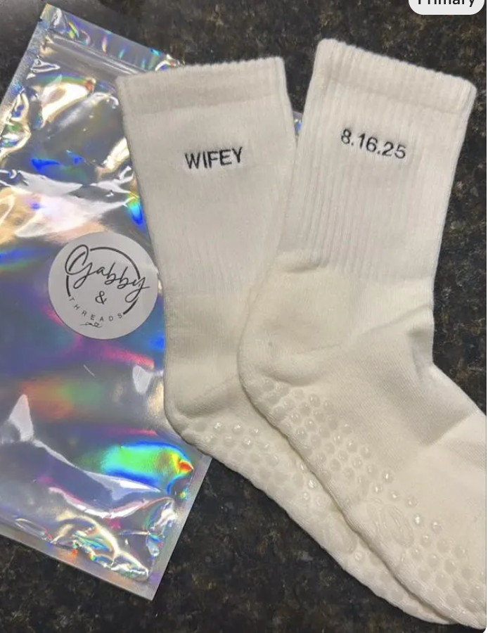 White grip socks with the word 'WIFEY' and the wedding date embroidered in blue thread