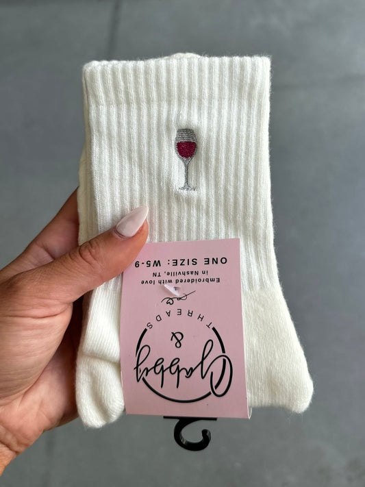 White sock with wine glass embroidery held by a hand against a gray background