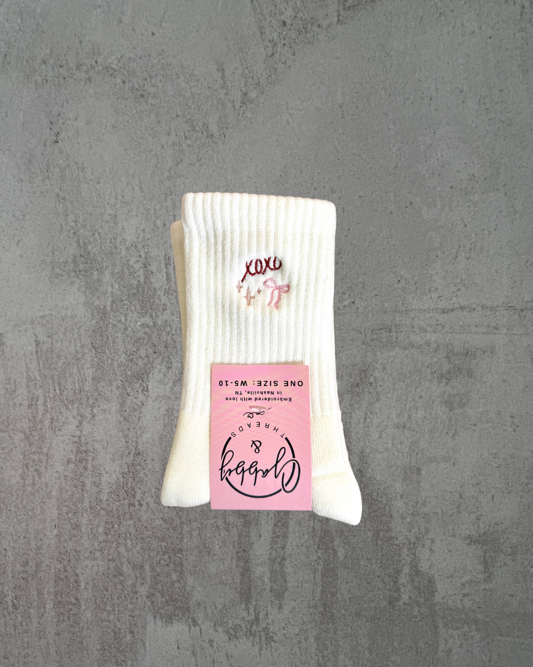 a pair of white grip socks with "xoxo," a sparkles and a bow