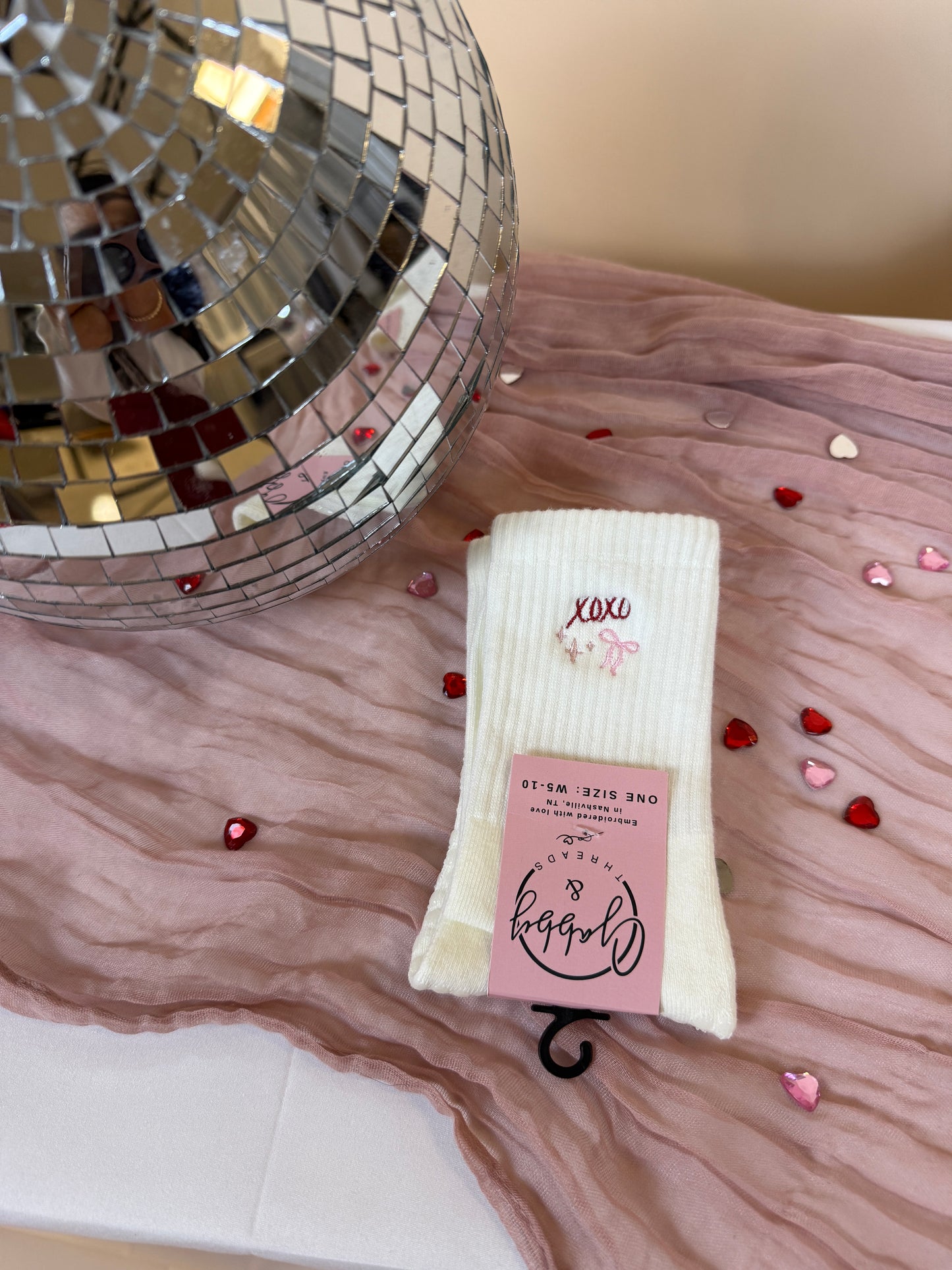 White grip sock with valentine's day embroidered design sits on a table with disco ball