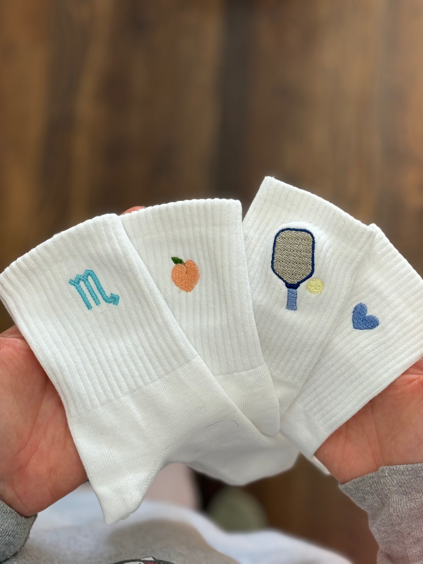 four pairs of socks with different embroidered icons(heart, pickleball paddle, peach and zodiac symbol)