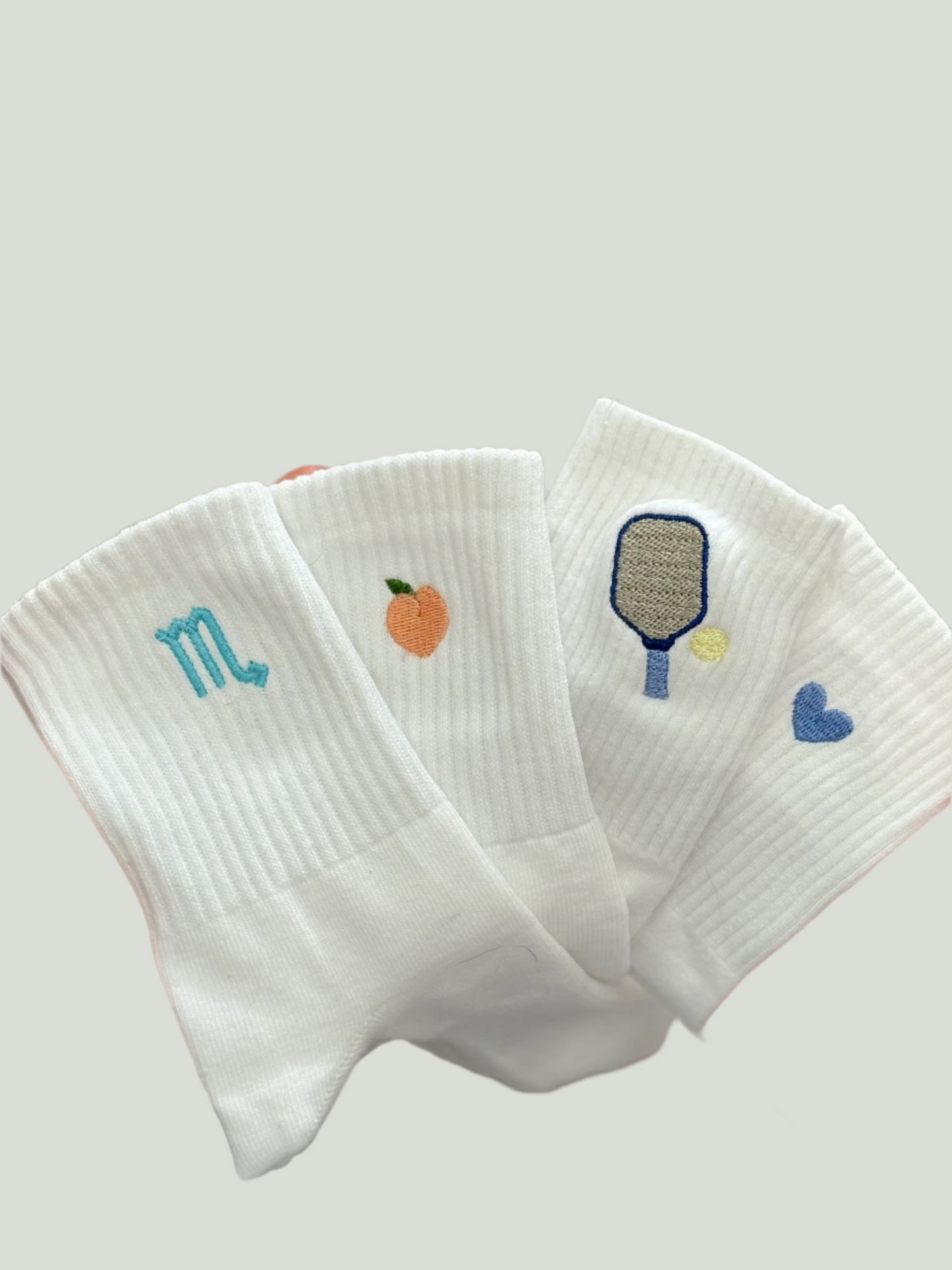 Four pairs of socks with different embroidered designs (zodiac symbol, peach, pickleball paddle and a heart).