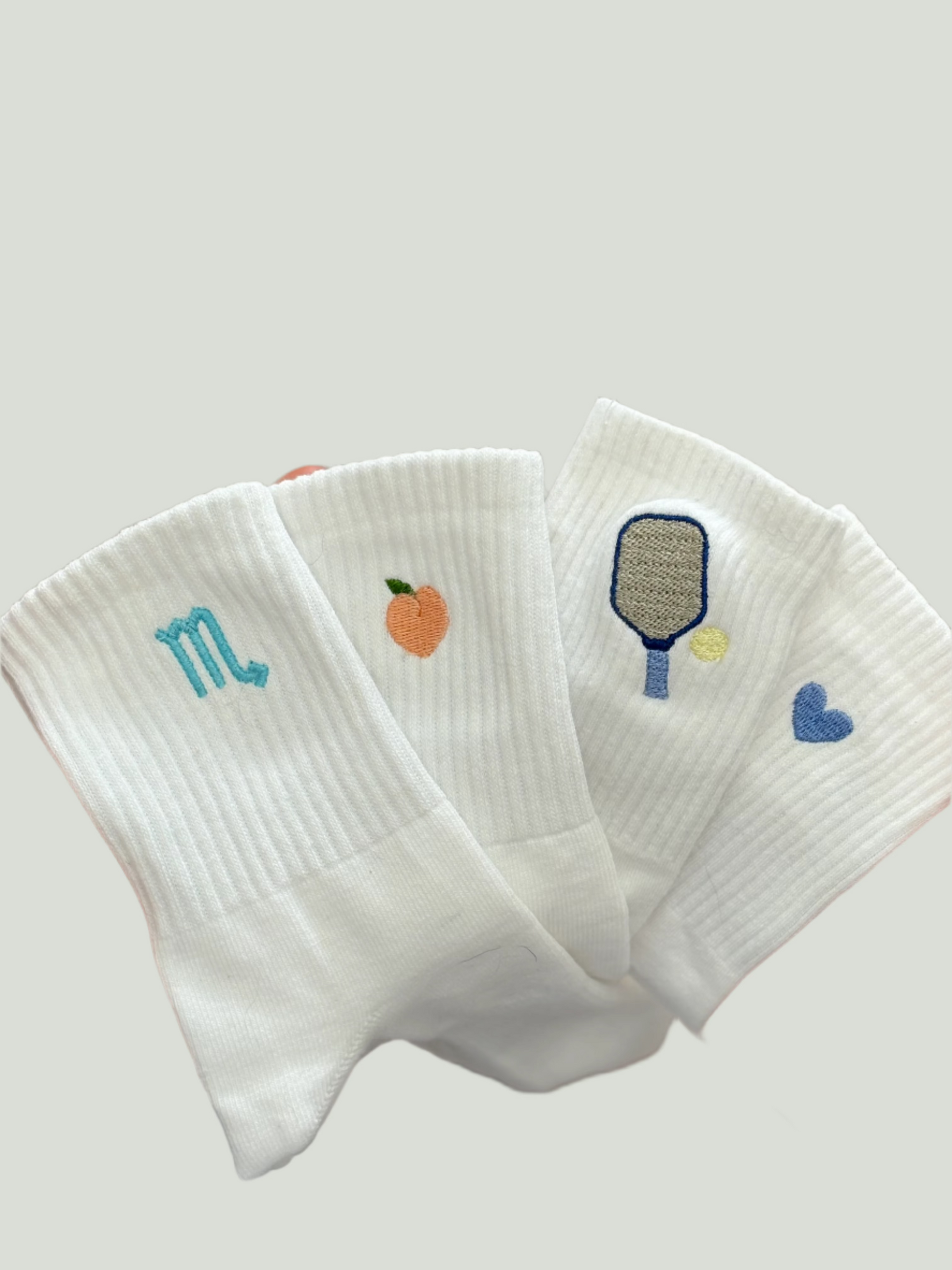 Four pairs of socks with different embroidered designs (zodiac symbol, peach, pickleball paddle and a heart).