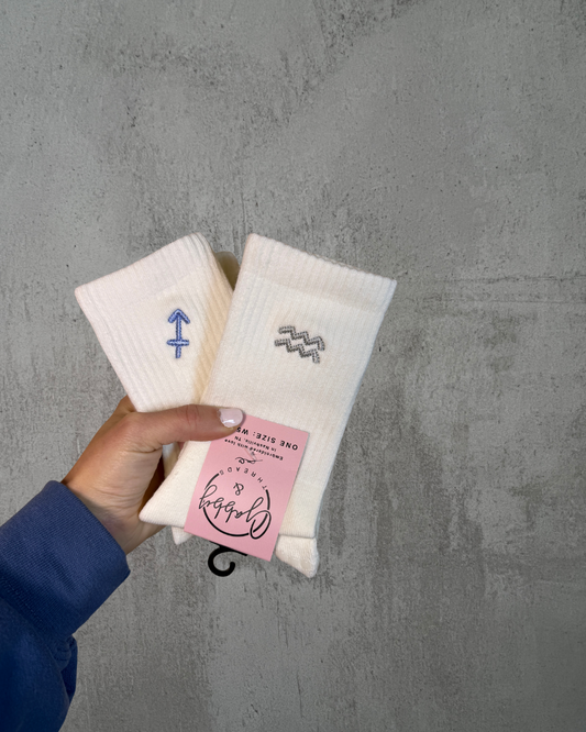 two pairs of white grip socks with embroidered zodiac symbols on them